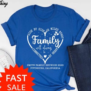 May include: A royal blue t-shirt with a white heart-shaped graphic that reads "Family will always be connected by heart." The shirt also includes text for the Smith Family Reunion 2025 in Pittsburg, California. A pair of dark blue jeans and white sneakers are also in the image.
