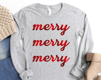 May include: A gray long-sleeved shirt with the words "merry merry merry" printed in red on the front. The shirt is styled with blue jeans, a beige beanie, and brown ankle boots.