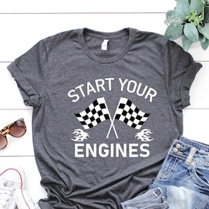 May include: A dark gray t-shirt with the text "Start Your Engines" in white lettering. The text is surrounded by two checkered flags and flames.