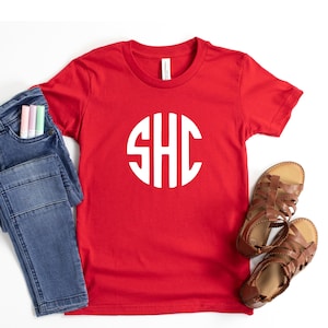 May include: Red short-sleeved t-shirt with a white circle monogram that says "SHC" on it.