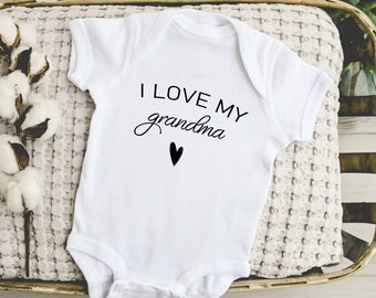 May include: White baby onesie with black text that reads "I love my grandma" with a small black heart below the text.