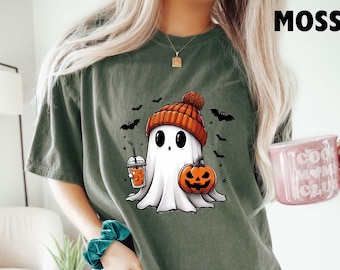 May include: A green t-shirt with a cartoon ghost wearing a hat and holding a pumpkin and a cup of coffee. The ghost is white and has a friendly face. The text "MOSS" is in the top right corner of the image.