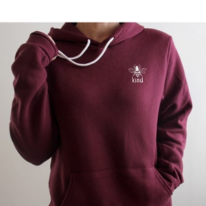May include: Burgundy hoodie with a white bee and the word "kind" embroidered on the front.