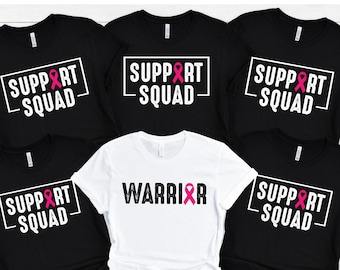 May include: Five black t-shirts with pink ribbon graphics and the text "Support Squad" and one white t-shirt with the text "Warrior" and a pink ribbon graphic.