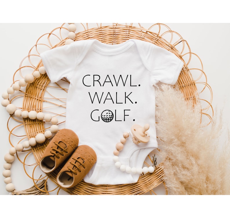 May include: White baby onesie with black text that reads "Crawl. Walk. Golf." and a golf ball graphic.
