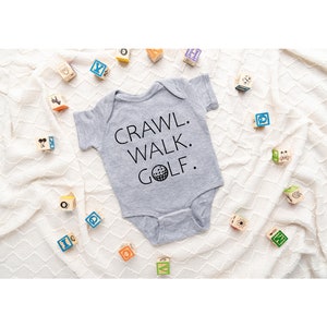 May include: Gray baby onesie with the text "CRAWL. WALK. GOLF." and a golf ball graphic.