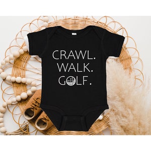 May include: Black baby onesie with white text that reads "Crawl. Walk. Golf." with a golf ball graphic.