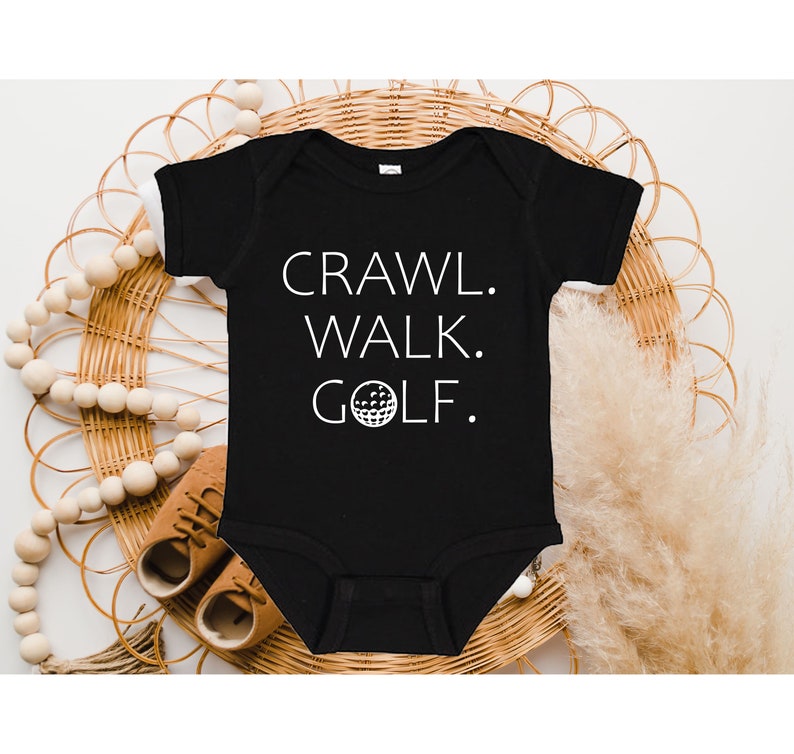 May include: Black baby onesie with white text that reads "Crawl. Walk. Golf." with a golf ball graphic.