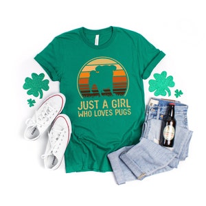 Peut inclure: T-shirt vert avec un graphique r&eacute;tro d'un carlin devant un coucher de soleil. Le texte "Just a girl who loves pugs" est imprim&eacute; sous le graphique.