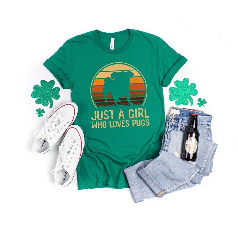 Peut inclure: T-shirt vert avec un graphique r&eacute;tro d'un carlin devant un coucher de soleil. Le texte "Just a girl who loves pugs" est imprim&eacute; sous le graphique.