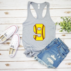 Puede incluir: Camiseta de tirantes gris con un n&uacute;mero 9 amarillo en la parte delantera. El n&uacute;mero est&aacute; bordeado de granate y tiene costuras granate que se asemejan a una pelota de b&eacute;isbol.
