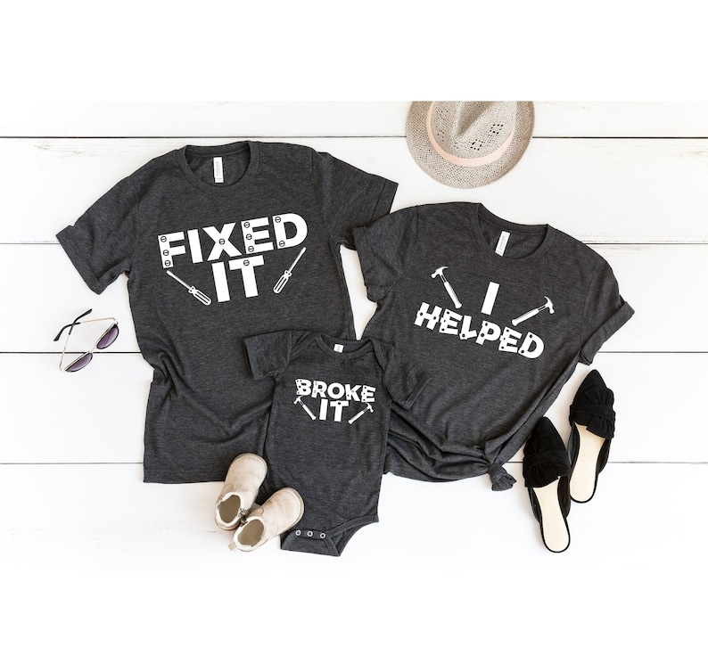 Puede incluir: Tres camisetas grises con texto blanco y gr&aacute;ficos. La camiseta m&aacute;s grande dice "Fixed It" con un destornillador y un tornillo. La camiseta mediana dice "I Helped" con dos martillos. La camiseta m&aacute;s peque&ntilde;a dice "Broke It" con un destornillador y un tornillo.
