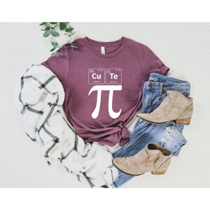 May include: A maroon t-shirt with a white graphic of the mathematical symbol pi and two periodic table elements: Cu (Copper) and Te (Tellurium).
