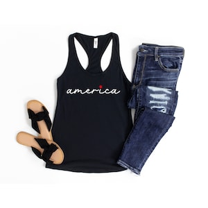 May include: A black tank top with a white cursive inscription that reads "america" with a small red star above the "a". The tank top is paired with blue jeans and brown sandals.