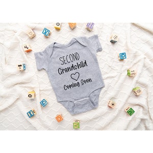 May include: A gray onesie with the text "Second Grandchild Coming Soon" and a heart symbol.