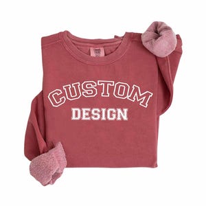 A red sweatshirt with the text "CUSTOM DESIGN" printed on it.