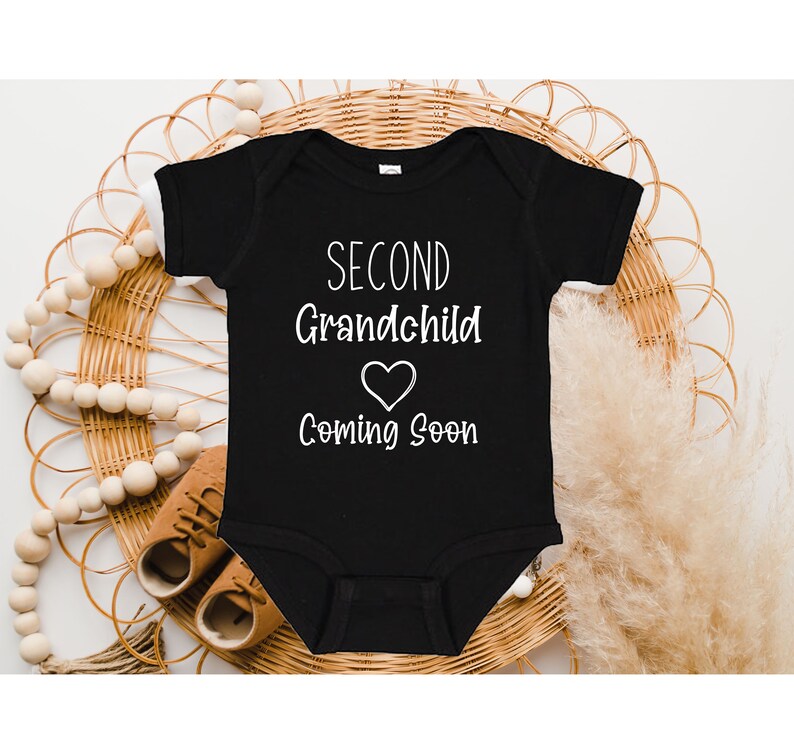 May include: Black baby onesie with white text that reads "Second Grandchild Coming Soon" with a heart symbol.