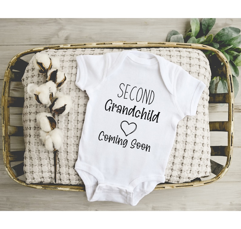 May include: White baby onesie with black text that reads "Second Grandchild Coming Soon" with a heart symbol.