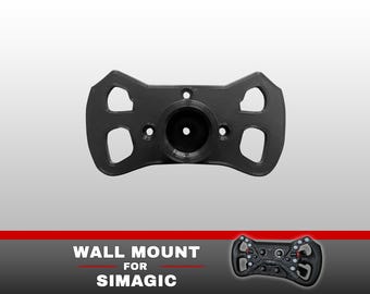 May include: A black plastic wall mount for a Simagic racing steering wheel. The mount features a central circular hub with a hollow core and four symmetrical cutouts on the sides. The text "WALL MOUNT FOR SIMAGIC" appears below the mount.