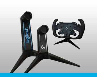 May include: Two black stands with blue and white accents, one featuring the word logitech and the other the G logo, alongside a black racing steering wheel controller with various buttons and a central G logo, all displayed against a plain background.