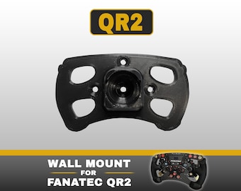 May include: A black, 3D-printed wall mount for a Fanatec QR2 steering wheel quick release system. The mount features a central circular opening and four mounting holes. Text at the top reads QR2, and text at the bottom reads WALL MOUNT FOR FANATEC QR2.