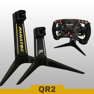 Może przedstawiać: Dwa czarne stojaki ekspozycyjne Fanatec z podstawami trójnożnymi oraz czarna kierownica wyścigowa z włókna węglowego zamontowana na trzecim stojaku. Wyższy stojak ma żółty napis Fanatec, a krótszy białe logo. Widoczny jest napis QR2.