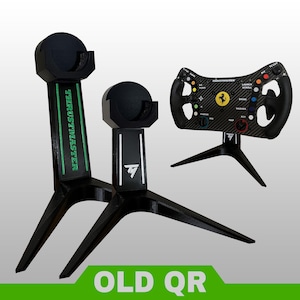 May include: Two black tripod stands for gaming steering wheels, one taller with green Thrustmaster branding and one shorter with a white TM logo, alongside a black carbon fiber textured Ferrari racing wheel with colorful buttons and a yellow logo.