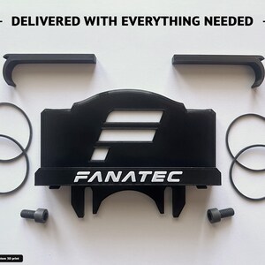 Op de afbeelding: Een zwarte 3D-geprinte Fanatec-accessoireset met een centrale montagebeugel met de tekst FANATEC, twee L-vormige clips, vier dunne zwarte rubberen O-ringen en twee grijze metalen bouten. De tekst DELIVERED WITH EVERYTHING NEEDED staat bovenaan.
