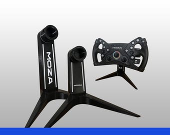 May include: Two black Moza branded stands with tripod bases and cylindrical mounts, positioned alongside a black Moza racing steering wheel featuring multiple buttons, rotary dials, and a central logo, all displayed against a plain background.