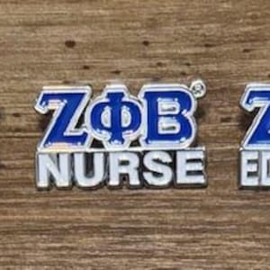 May include: Three pins with the letters ZΦB in blue and white. Each pin has a different profession: Therapist, Nurse, and Educator. The pins are on a wooden surface.