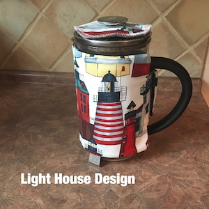 Puede incluir: Una cafetera de prensa aislada blanca y roja con un diseño de faro. La cafetera tiene un asa negra y una jarra de vidrio transparente. El texto "Light House Design" está impreso debajo de la cafetera.