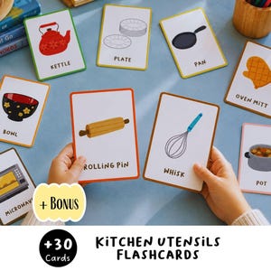 May include: A set of educational flashcards featuring illustrations of kitchen items including a red kettle, plate, pan, oven mitt, bowl, rolling pin, whisk, microwave, and pot, with each card labeled with its corresponding name in black text.
