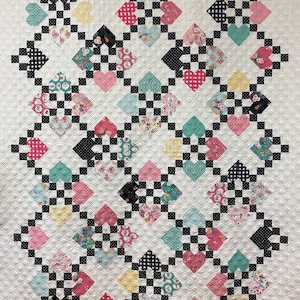 May include: A quilt with a white background and a black and white chequered pattern. The quilt is decorated with a variety of colourful hearts, each with a different floral pattern.