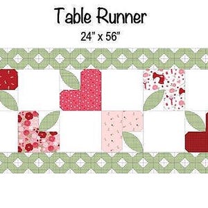 May include: A rectangular table runner measuring 24" x 56" featuring a green and white chequered border. The centre displays a repeating pattern of red and pink heart-shaped motifs with light green leaves, arranged against a white background.