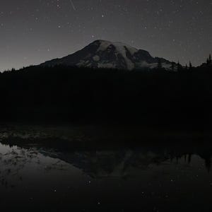 Peut inclure: Paysage nocturne sombre avec une montagne enneigée sous un ciel étoilé. La montagne se reflète dans une étendue d'eau sombre. L'image a une esthétique sombre et une ambiance mystérieuse, avec le texte "WRIGHT AROUND THE BEND" en cercle.