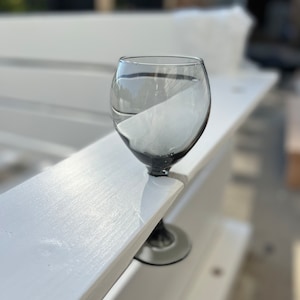 Op de afbeelding: Een helder glazen wijnglas met een zwarte steel en voet, dat op een wit houten oppervlak staat.