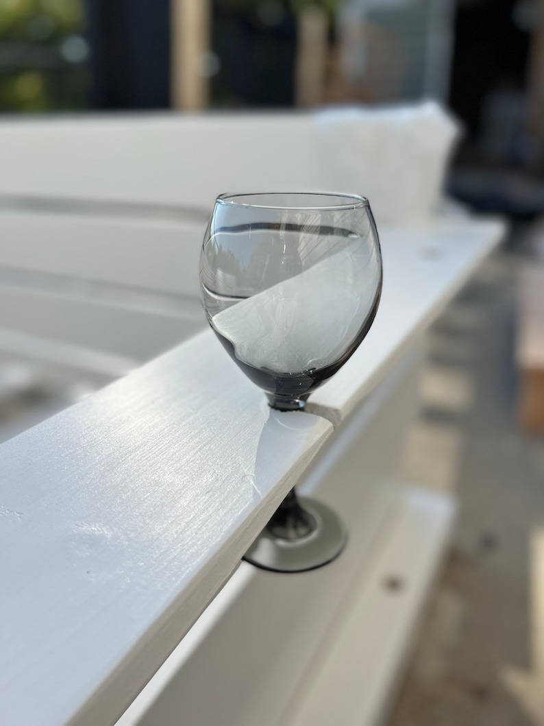 Op de afbeelding: Een helder glazen wijnglas met een zwarte steel en voet, dat op een wit houten oppervlak staat.