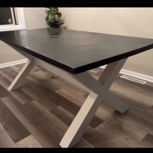 May include: A black table top with a white X-shaped base. The table is made of wood and has a smooth, polished finish.