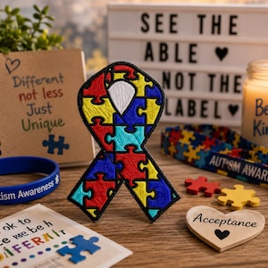 May include: An embroidered awareness ribbon patch featuring a colorful puzzle piece pattern in red, yellow, blue, and teal. The patch is surrounded by items including a notebook with the text Different not less Just Unique, a candle, and a lanyard.