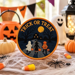 May include: A circular patch with the words "TRICK OR TREAT" in gold lettering. The patch features a Halloween scene with three trick-or-treaters, a house, trees, and a full moon. The patch is surrounded by orange thread.