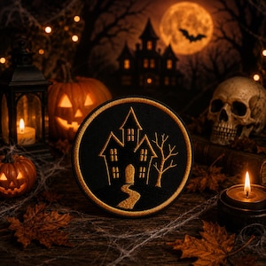 May include: A circular embroidered patch featuring a black background with a gold-stitched haunted house, a winding path, and a bare tree. The patch has a thick gold border and is displayed against a dark, atmospheric Halloween-themed backdrop.