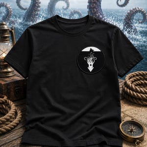 May include: A black short-sleeve t-shirt featuring a circular patch on the left chest. The patch displays a white graphic of a sea creature with long tentacles extending downward from a small boat silhouette against a solid black background.