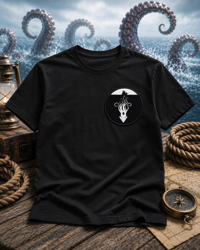 May include: A black short-sleeve t-shirt featuring a circular patch on the left chest. The patch displays a white graphic of a sea creature with long tentacles extending downward from a small boat silhouette against a solid black background.