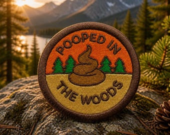 May include: Round embroidered patch with the text "POOPED IN THE WOODS". The patch features a brown poop emoji, green trees, and an orange and yellow background. The patch is set against a scenic mountain backdrop.