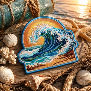 May include: A semi-circular embroidered patch featuring a detailed ocean wave crashing against a sandy shore under a bright yellow sun. The design uses shades of blue, white, and gold thread with a distinct blue border outlining the entire shape.
