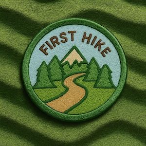 May include: Embroidered patch with the words "FIRST HIKE" in brown, featuring a mountain scene with trees and a winding path. The patch has a green border and is set against a green textured background.