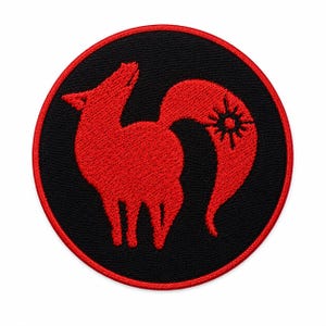 Pode incluir: Um emblema bordado circular com fundo preto e borda vermelha. O centro exibe a silhueta estilizada de uma raposa vermelha de perfil, voltada para a esquerda com a cabe&ccedil;a inclinada para cima. Um s&iacute;mbolo de sol est&aacute; integrado na cauda da raposa.