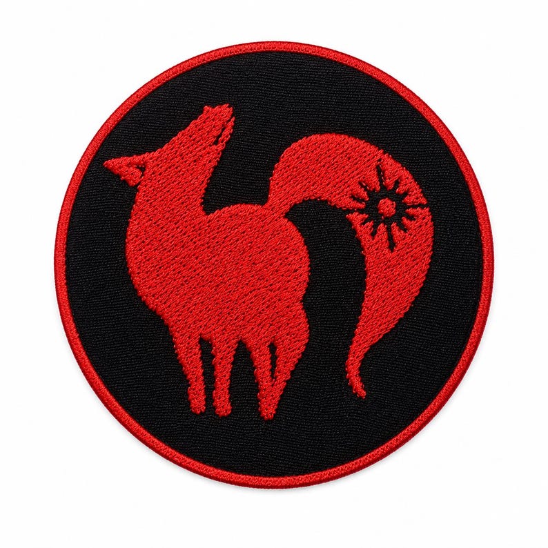 Pode incluir: Um emblema bordado circular com fundo preto e borda vermelha. O centro exibe a silhueta estilizada de uma raposa vermelha de perfil, voltada para a esquerda com a cabe&ccedil;a inclinada para cima. Um s&iacute;mbolo de sol est&aacute; integrado na cauda da raposa.