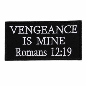 Op de afbeelding: Zwarte rechthoekige patch met wit geborduurde tekst. De tekst luidt "VENGEANCE IS MINE Romans 12:19". De patch heeft een zwarte rand en is waarschijnlijk gemaakt van stof.