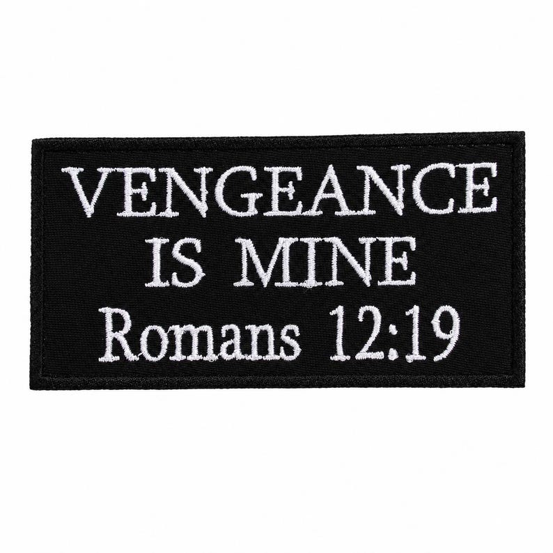 Op de afbeelding: Zwarte rechthoekige patch met wit geborduurde tekst. De tekst luidt "VENGEANCE IS MINE Romans 12:19". De patch heeft een zwarte rand en is waarschijnlijk gemaakt van stof.